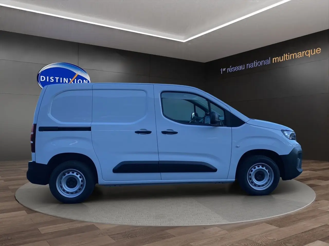 Vue latérale droite d'un utilitaire Peugeot Partner blanc avec protections noires et jantes acier en showroom.