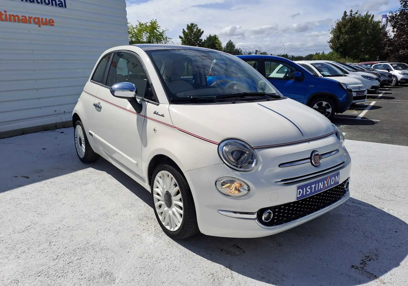 Fiat 500 blanche vue 3/4 avant droit avec ligne rouge décorative et jantes blanches élégantes.