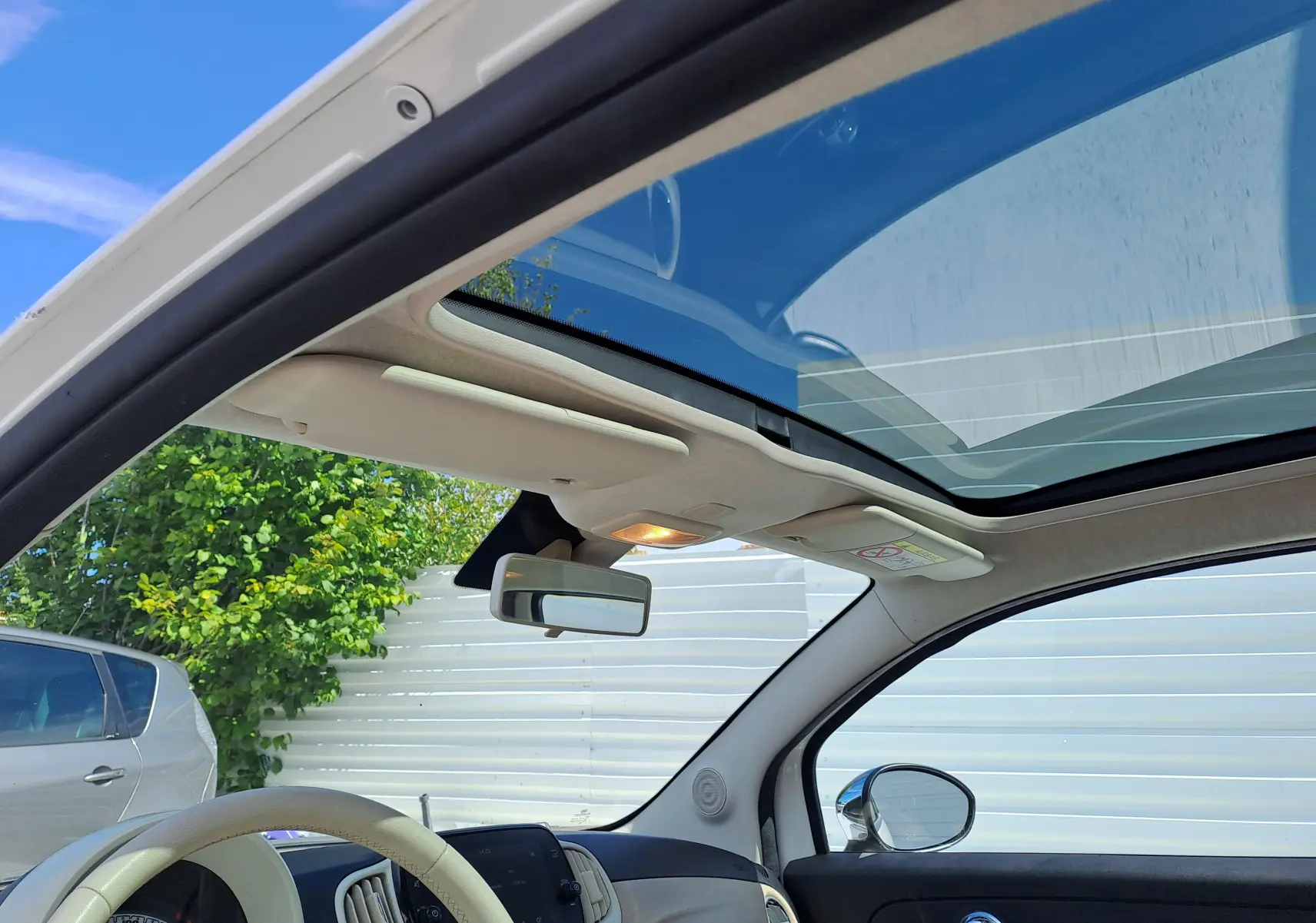 Vue intérieure avant de la FIAT 500 blanche 2022, toit panoramique ouvert et volant beige visible.