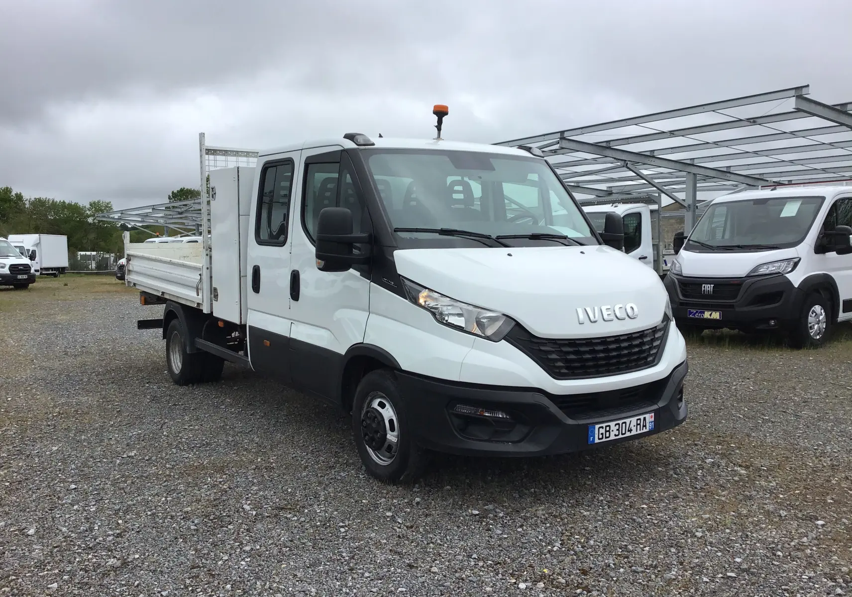 IVECO Daily Chassis double cabine blanc vu en 3/4 avant droit, avec benne, coffre latéral et roues jumelées.