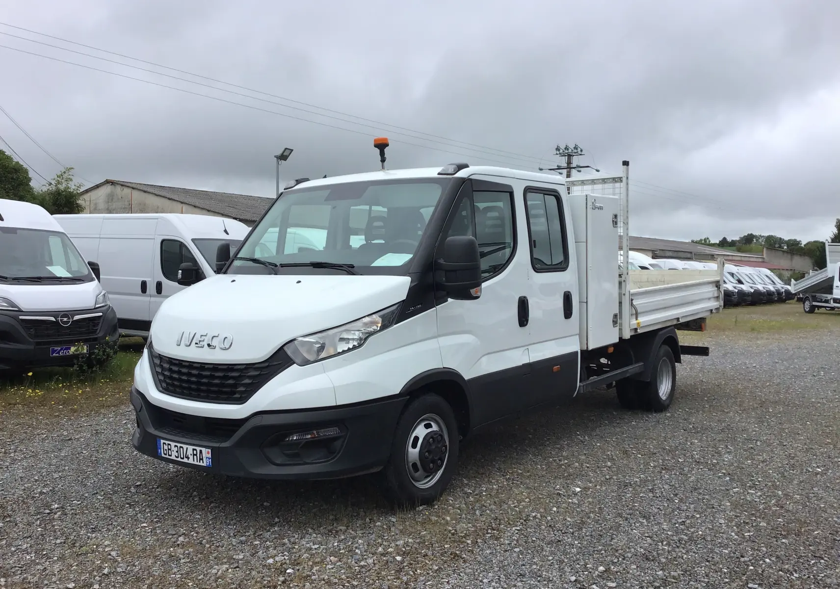 IVECO Daily Chassis double cabine blanc vu en 3/4 avant droit avec benne et coffre sur parking.