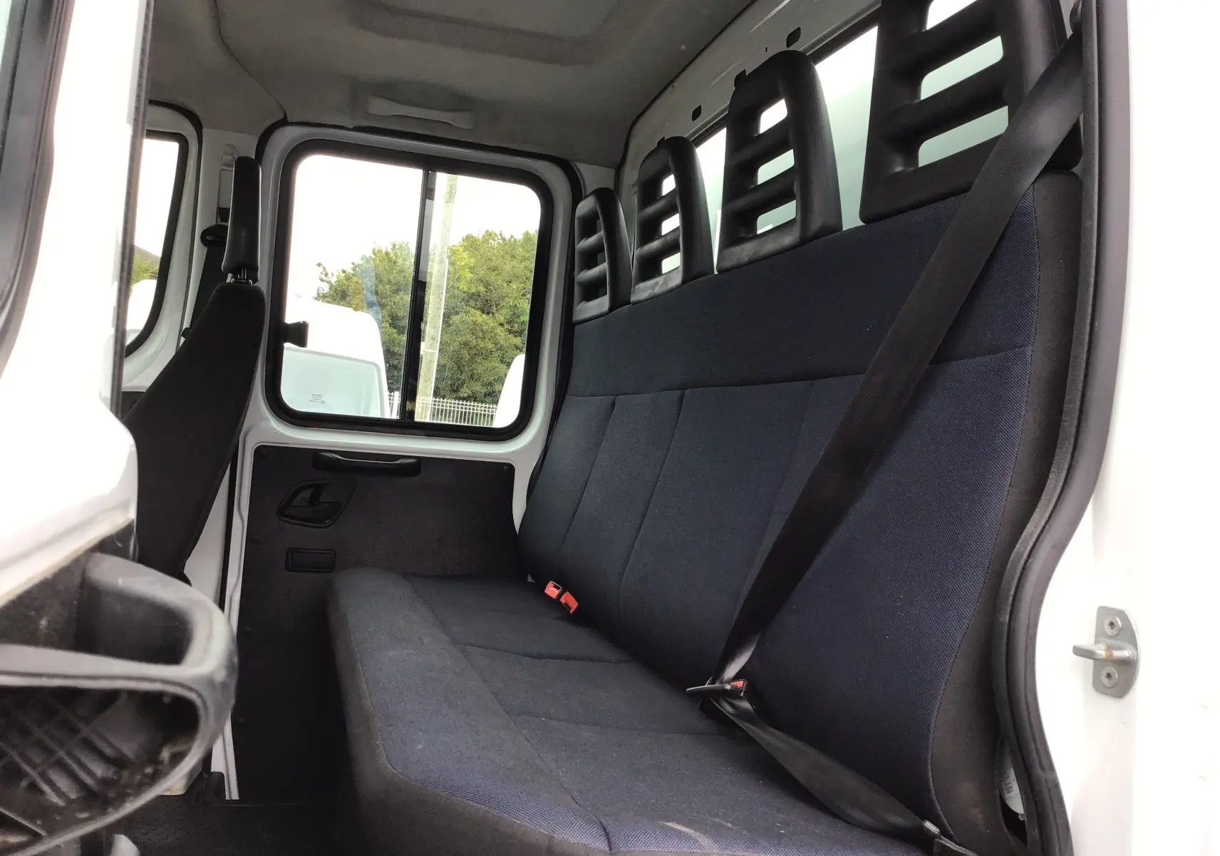 Vue intérieure de la cabine arrière du Daily Iveco blanc, montrant la banquette noire avec ceintures de sécurité.