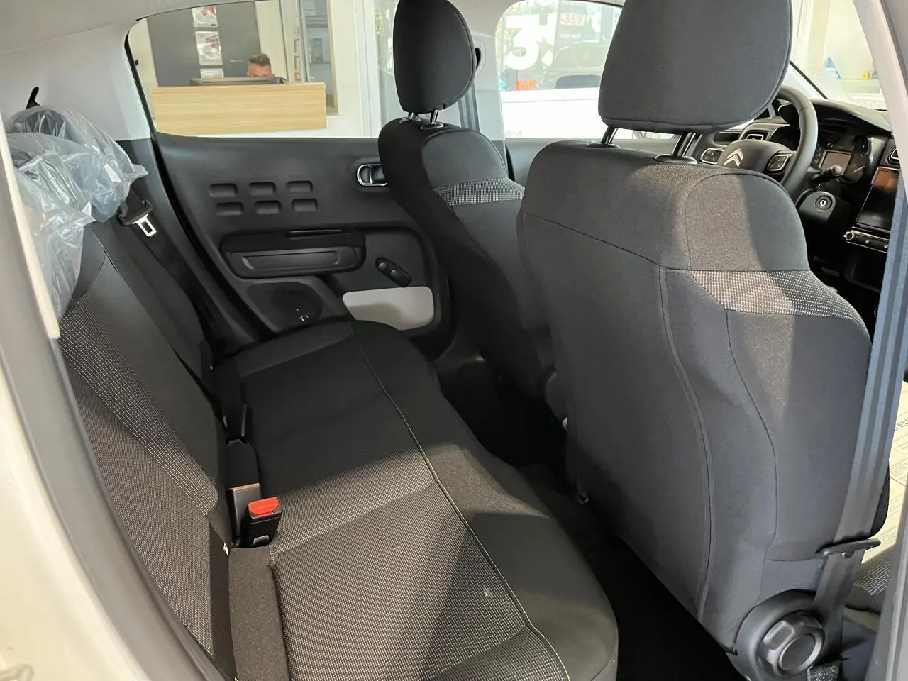 Vue intérieure arrière droite de la Citroën C3 blanche 2024, sièges tissu gris avec surpiqûres jaunes et accoudoirs textiles.