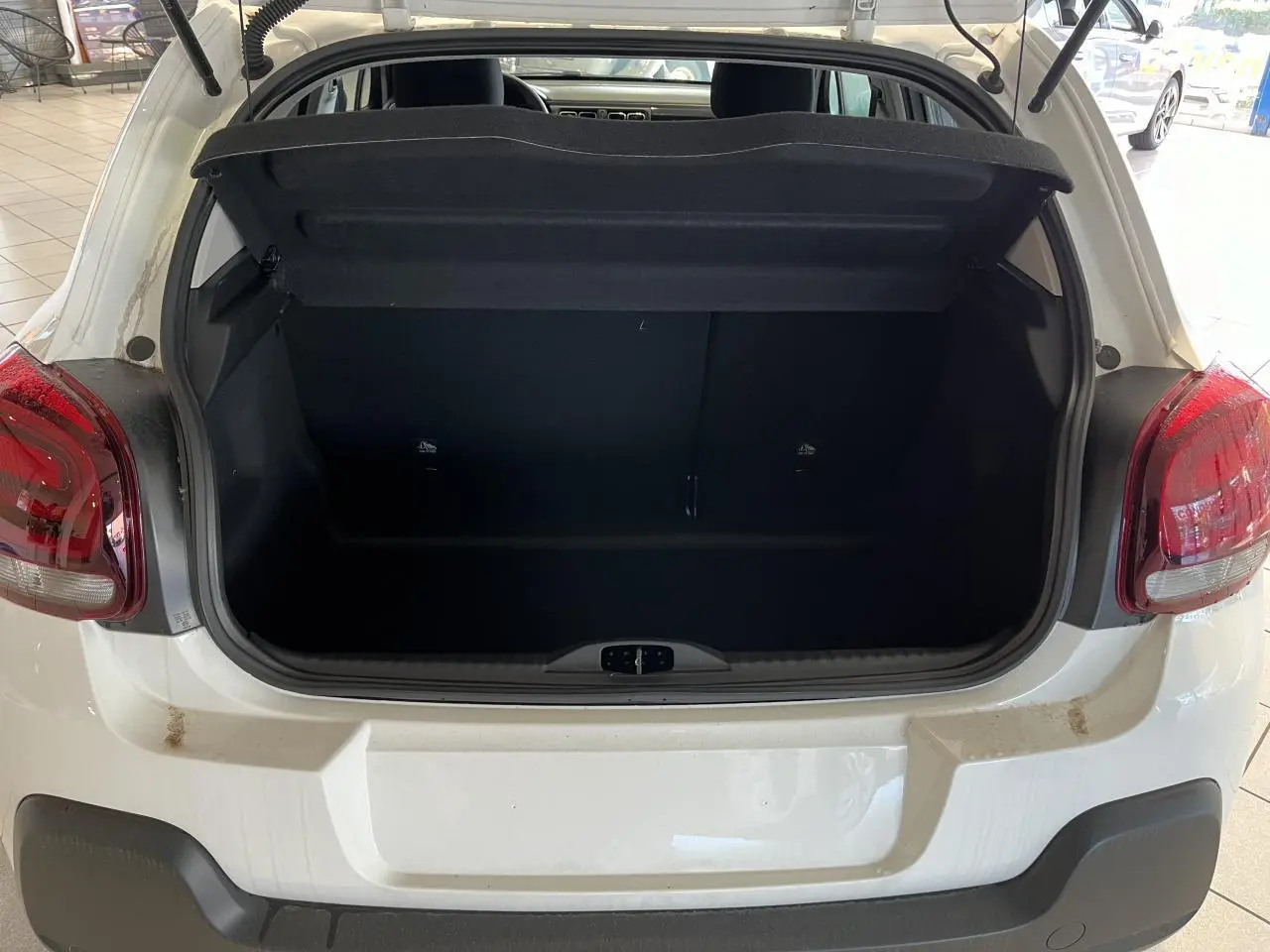 Coffre ouvert d'une Citroën C3 blanche vue de l'arrière, avec feux arrière rouges et pare-chocs noir mat.