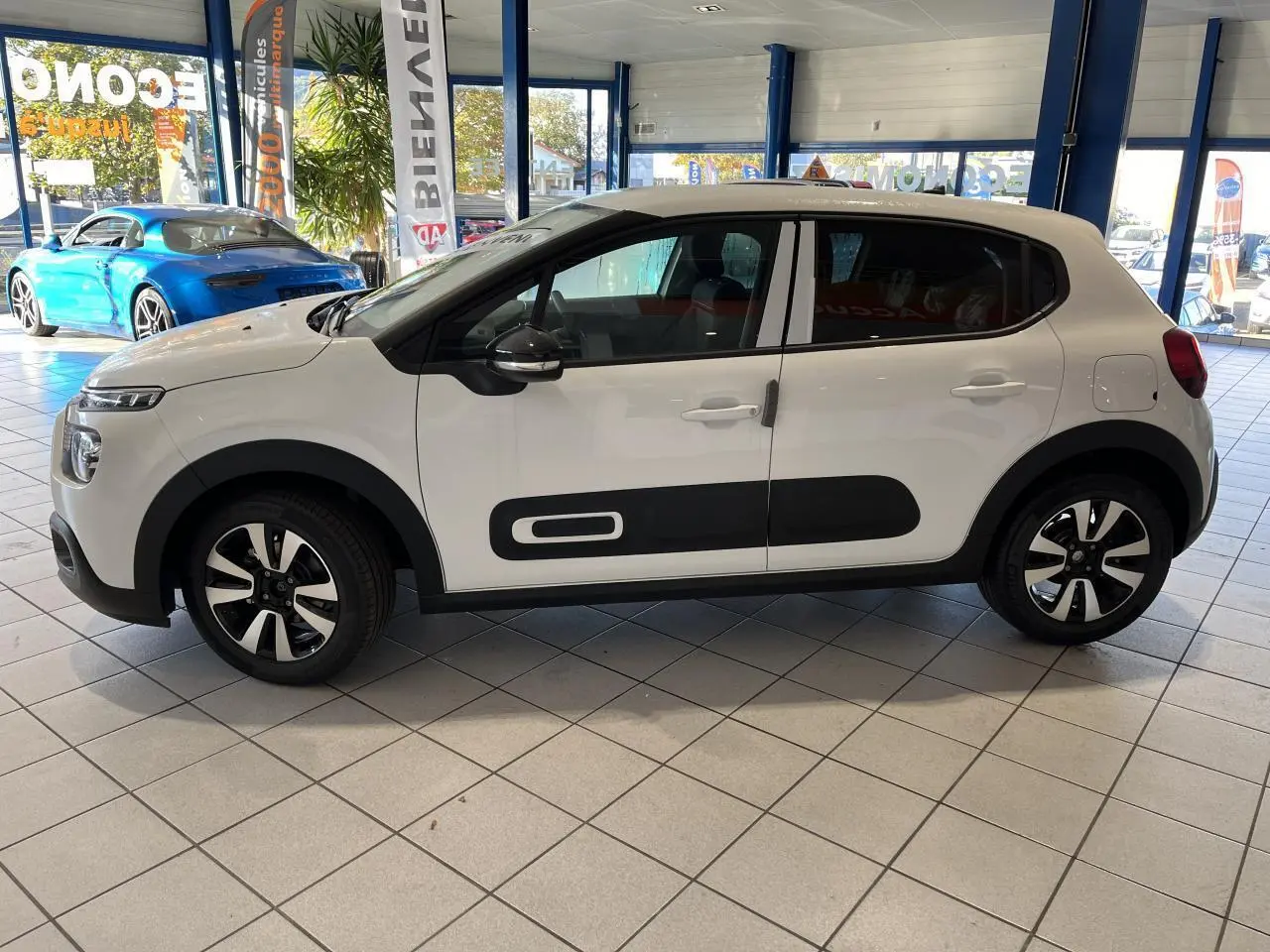 Profil droit d'une Citroën C3 blanche avec protections latérales noires et jantes alliage en showroom.