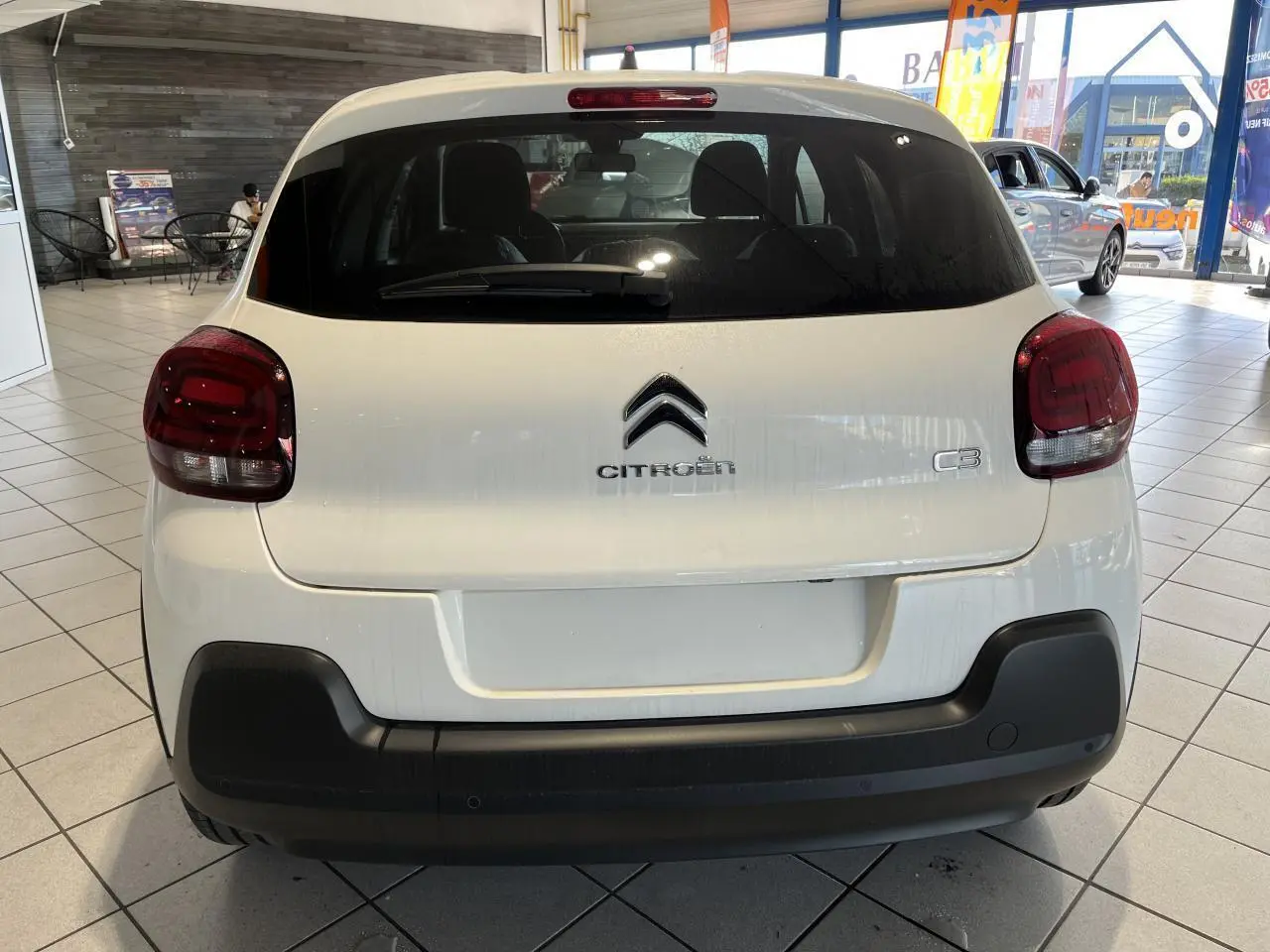 Vue arrière d'une Citroën C3 blanche avec feux arrière rouges et pare-chocs noir mat en showroom.