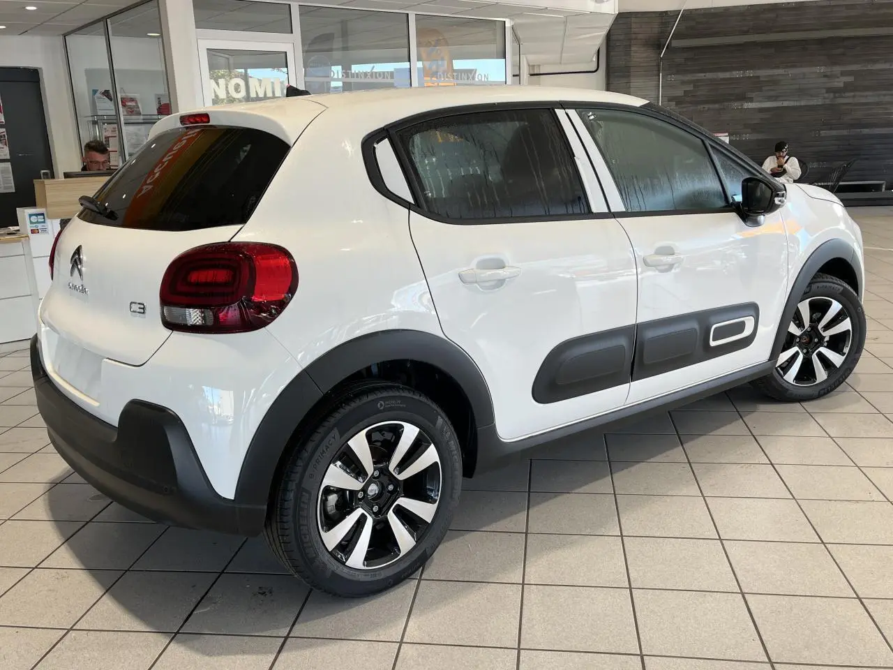 Vue 3/4 arrière droite d'une Citroën C3 blanche avec protections latérales noires et jantes alliage diamantées.