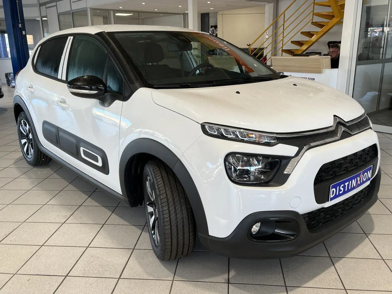 Citroën C3 blanc banquise vue 3/4 avant droit avec Airbump noir et coques de rétroviseurs noires dans un showroom.