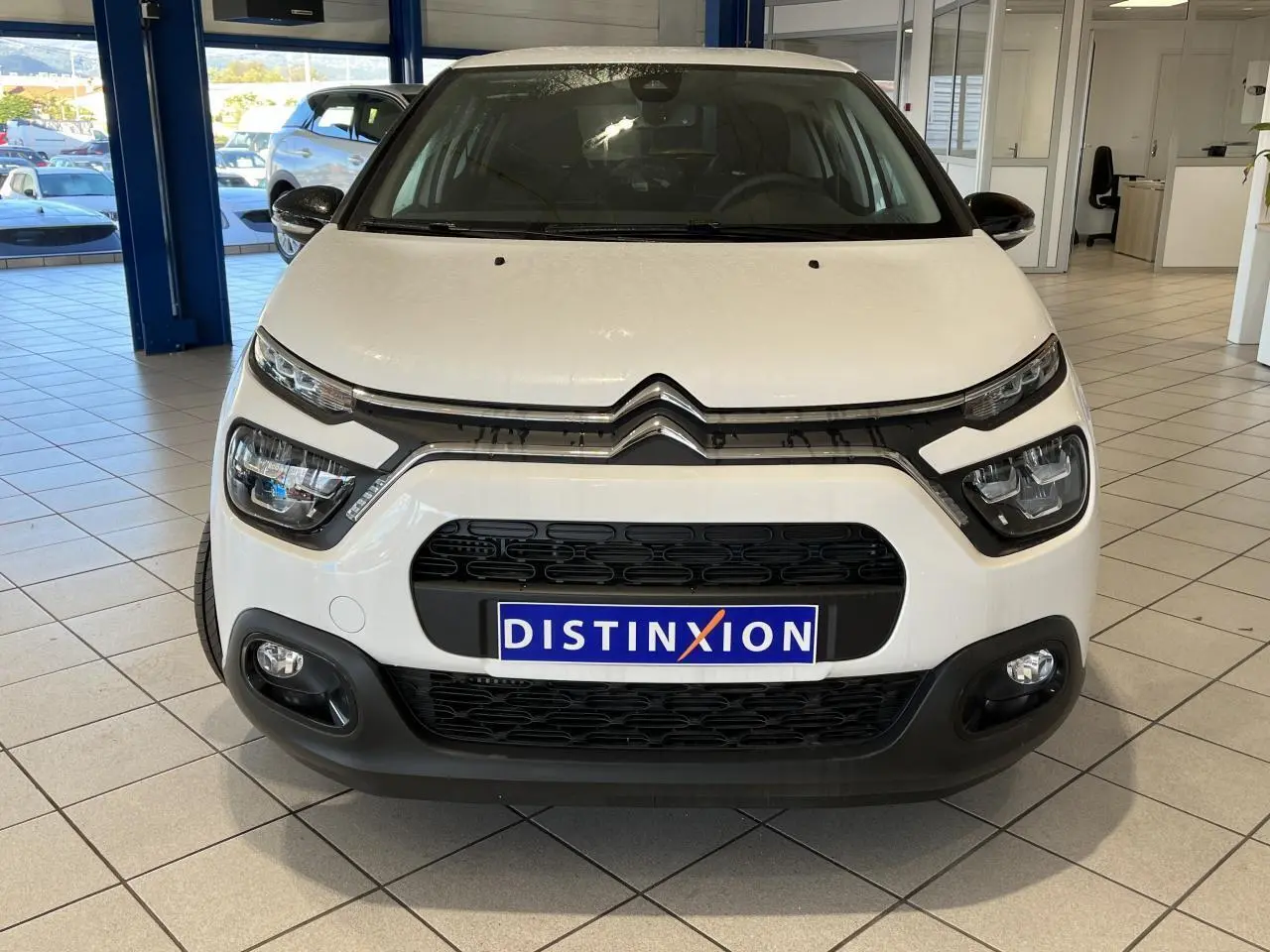 Vue frontale d'une Citroën C3 blanche avec calandre noire et feux LED dans un showroom lumineux.