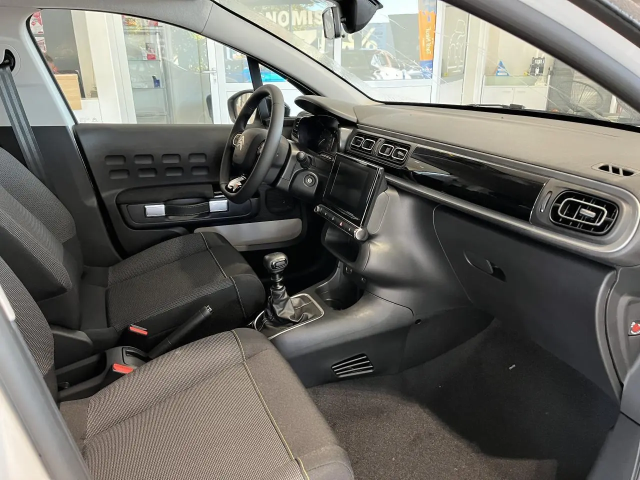 Intérieur avant droit de la Citroën C3 2024 avec tableau de bord noir brillant et sièges tissu gris foncé.