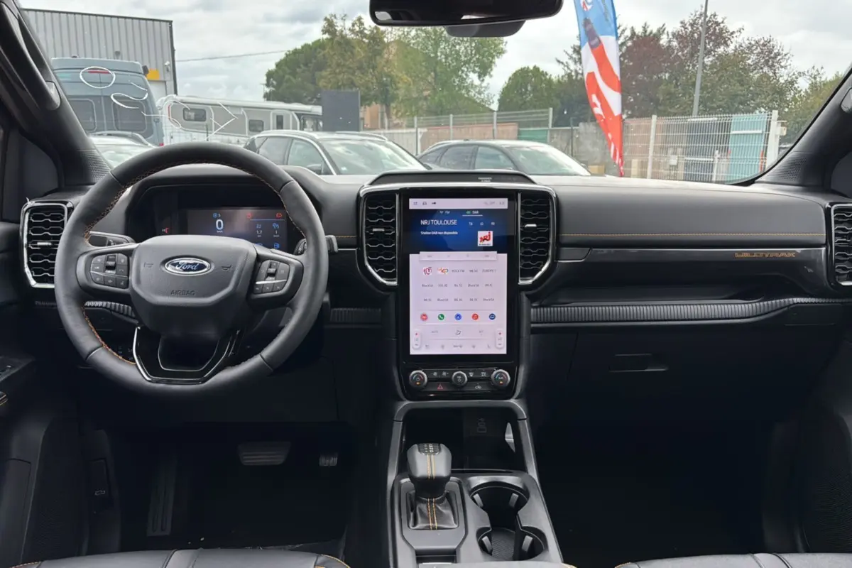 Intérieur du Ford Ranger 2025 Wildtrak Plus noir agate, vue frontale du tableau de bord avec écran tactile vertical et volant cuir.