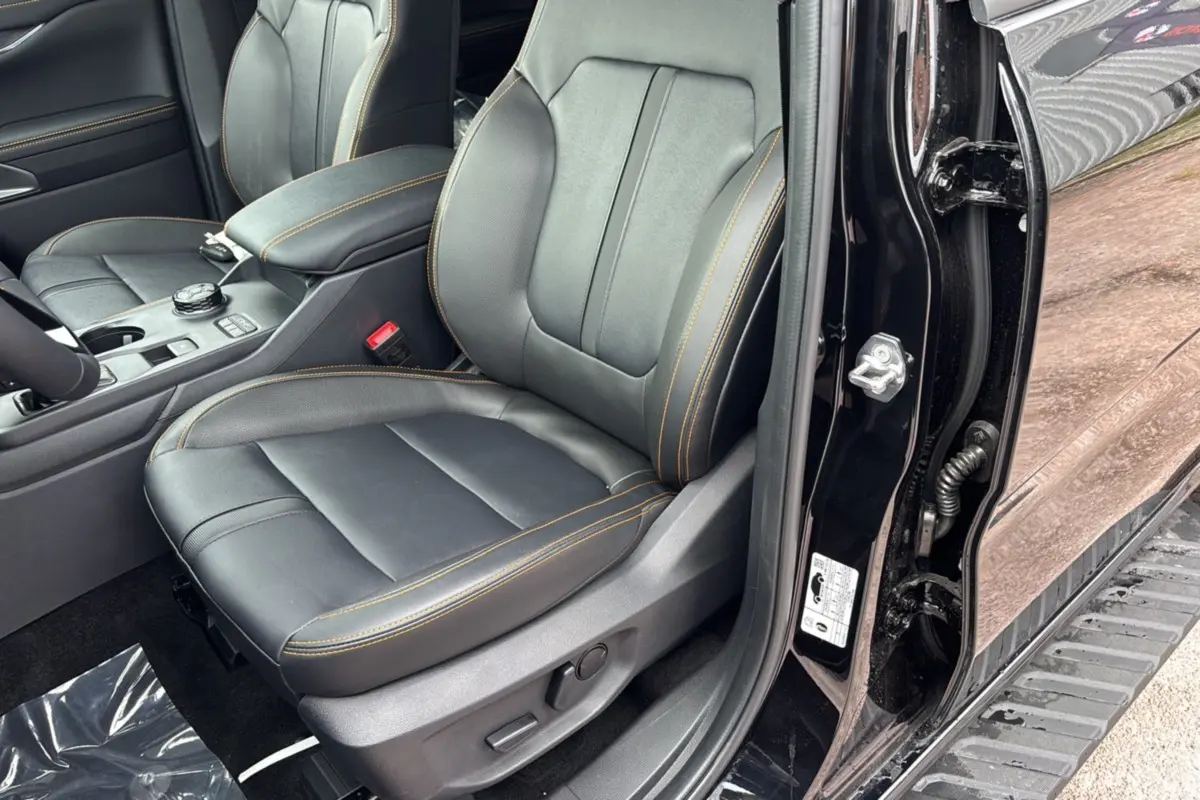 Vue intérieure côté conducteur du Ford Ranger 2025 noir agate, sièges cuir noirs avec surpiqûres orange et console centrale visible.