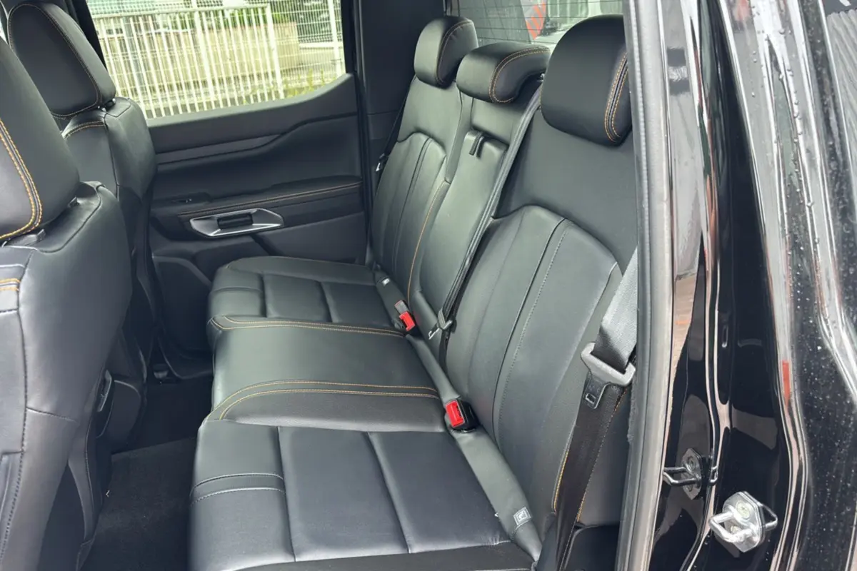 Vue intérieure arrière du Ford Ranger 2025 noir agate, sièges en cuir noir avec surpiqûres orange Wildtrak Plus.