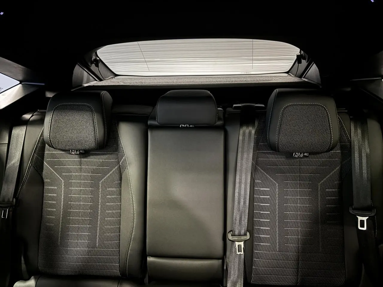 Vue arrière intérieure des sièges arrière noirs du Peugeot 3008 Hybrid 2025 avec appuie-têtes et ceintures visibles.