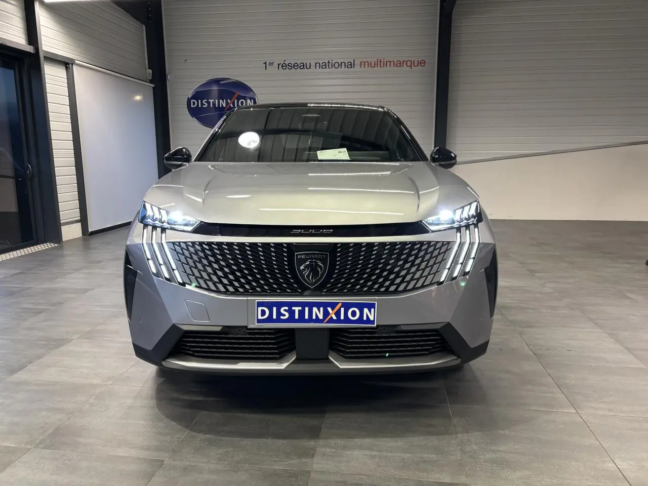 Vue frontale du Peugeot 3008 gris Artense avec calandre noire laquée et feux LED à griffes allumés dans un showroom.