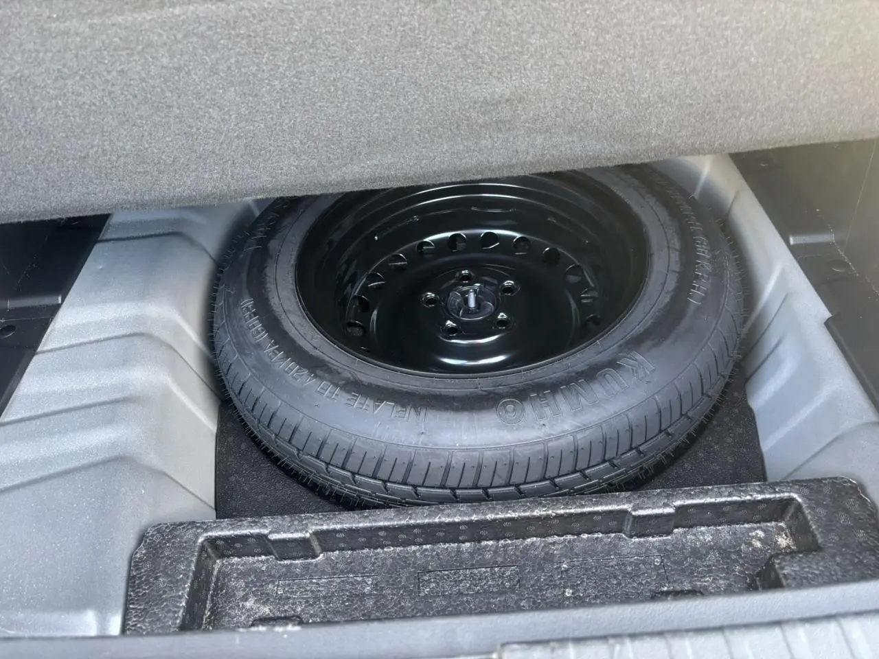 Vue rapprochée de la roue de secours temporaire noire dans le coffre d'un Renault Arkana gris métallisé.