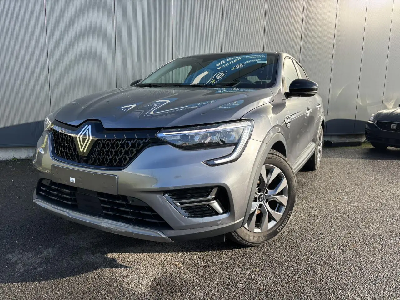 Vue 3/4 avant d’un Renault Arkana gris métallisé avec calandre noire et jantes alliage grises sur un sol asphalté.