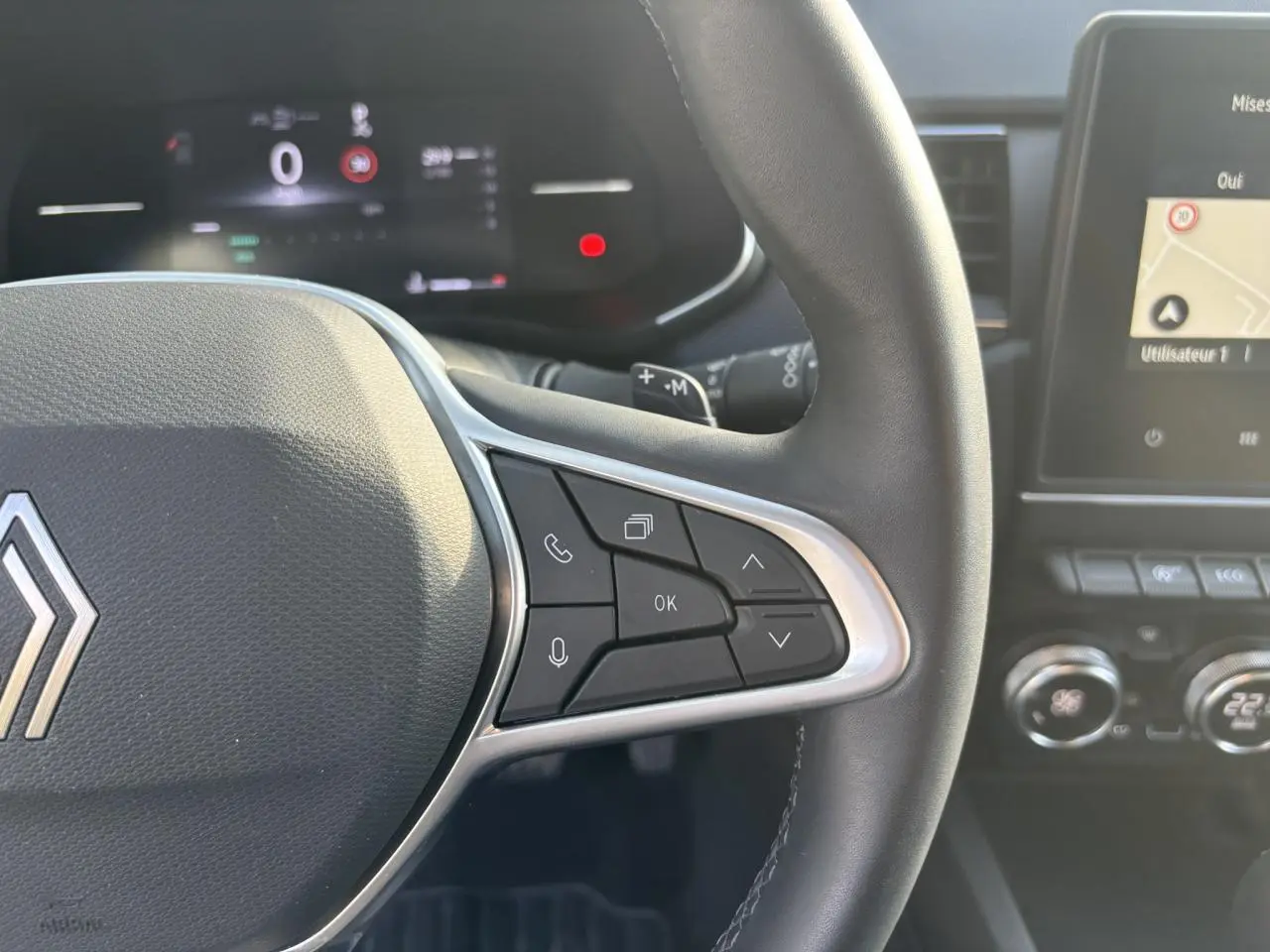 Gros plan sur le volant noir et les commandes multifonctions côté droit du Renault Arkana 2025, avec écran tactile en arrière-plan.