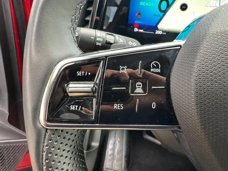 Gros plan sur les commandes au volant côté gauche du Renault Austral Rouge Flamme 2025 avec affichage numérique en arrière-plan.