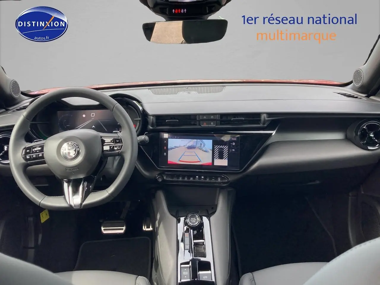 Vue intérieure frontale de l'Alfa Romeo Junior 1.2 hybride 2026, tableau de bord noir avec écran tactile et caméra de recul affichée.