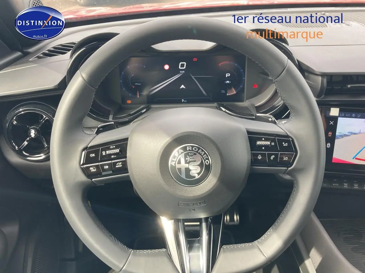 Vue centrée sur le volant noir de l'Alfa Romeo Junior 1.2 hybride 2026, avec tableau de bord numérique et écran tactile visible.