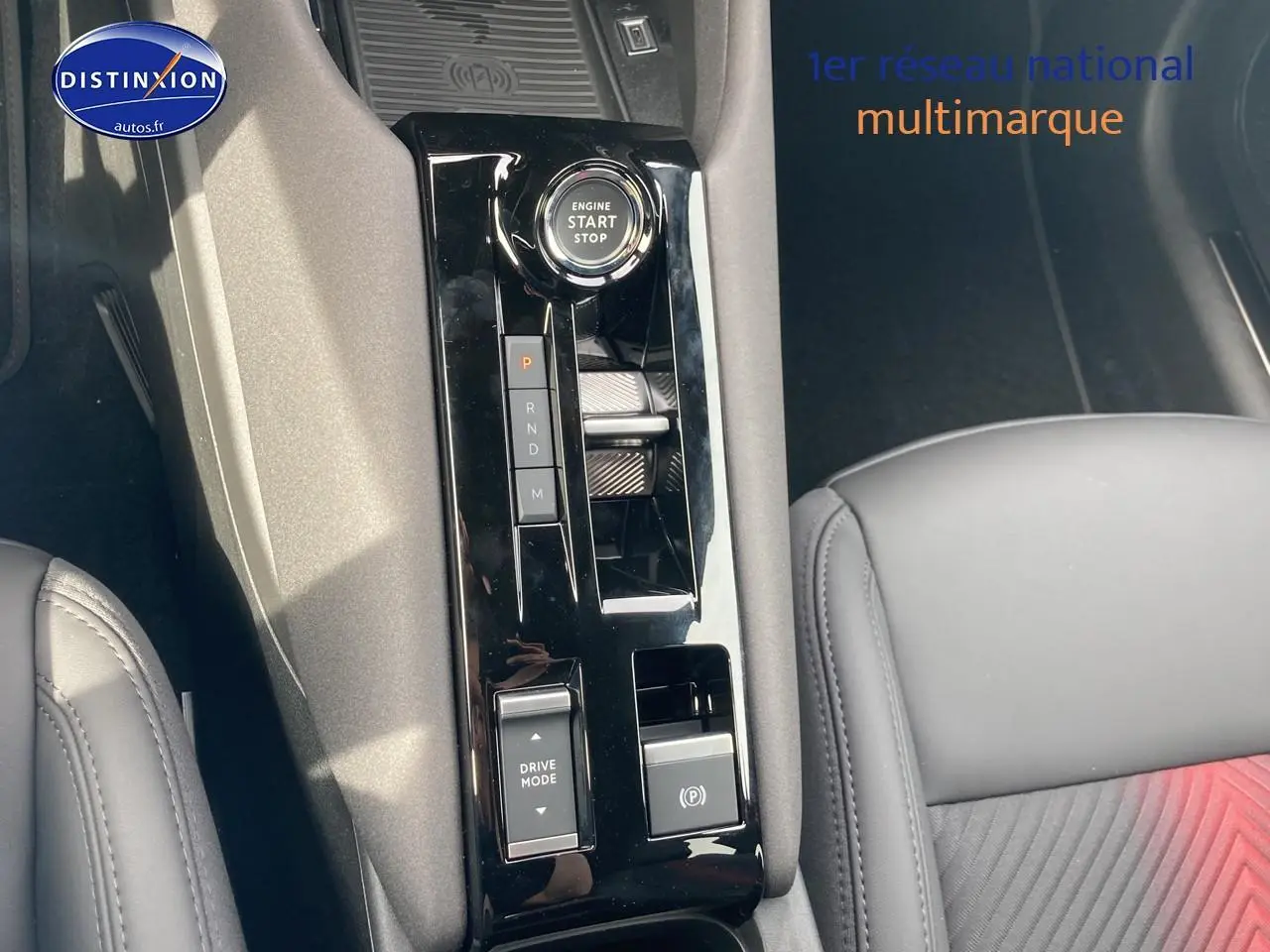 Vue rapprochée de la console centrale noire brillante de l'Alfa Romeo Junior 1.2 hybride, avec siège cuir noir partiel visible.