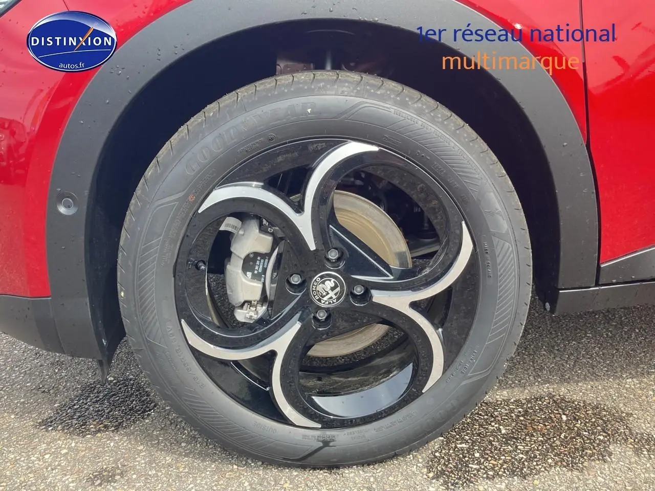 Gros plan sur la roue avant gauche d'une Alfa Romeo Junior 1.2 hybride rouge et noir, avec jante alliage noire et argentée.