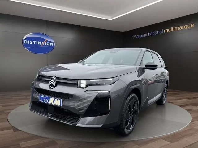 Vue 3/4 avant d'une Citroën C5 hybride gris foncé avec phares LED et jantes noires dans un showroom.