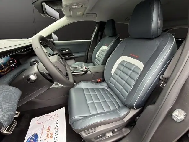 Vue intérieure côté conducteur de la Citroën C5 Hybride 2026, sièges cuir gris foncé avec surpiqûres blanches et tableau de bord moderne.