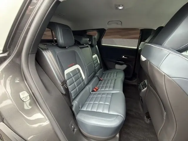 Vue intérieure arrière gauche des sièges en cuir gris foncé de la Citroën C5 Hybride 2026 avec surpiqûres et ceintures rouges.
