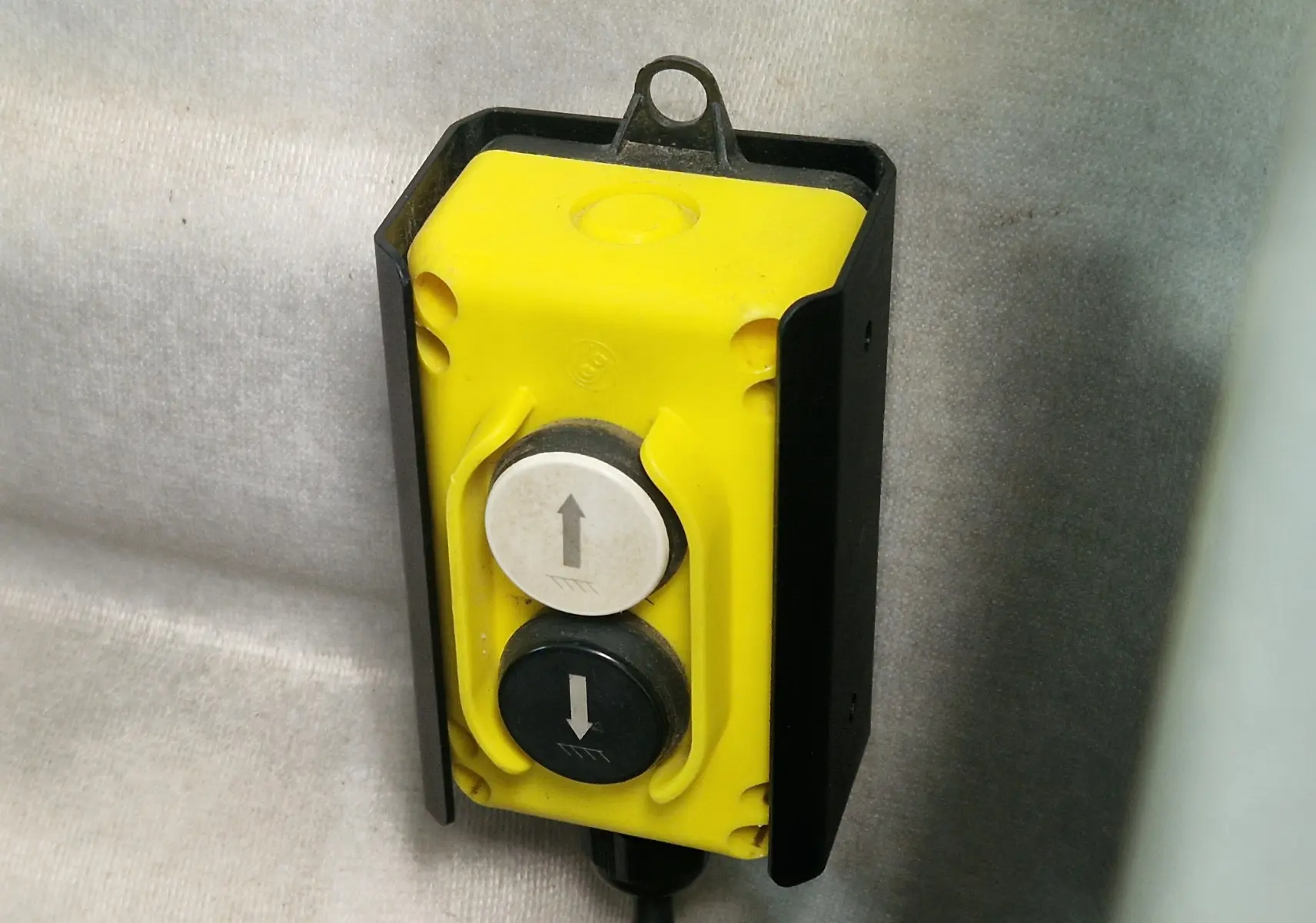 Bouton de commande jaune avec deux touches fléchées, détail d'un équipement du Renault Master Benne blanc vu de face.