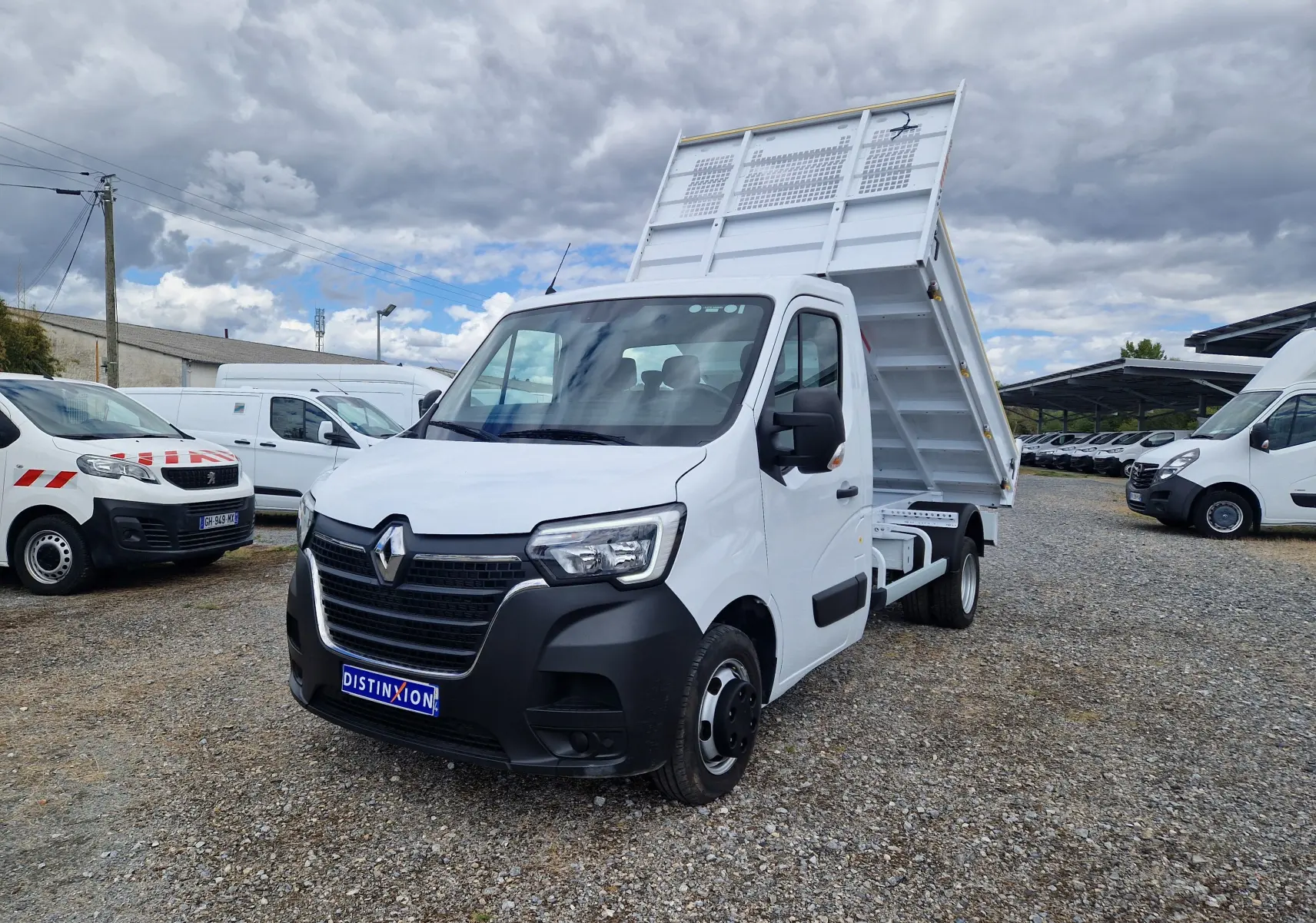 Renault Master Benne blanc vu en 3/4 avant droit, benne relevée et roues jumelées visibles sur terrain gravillonné.