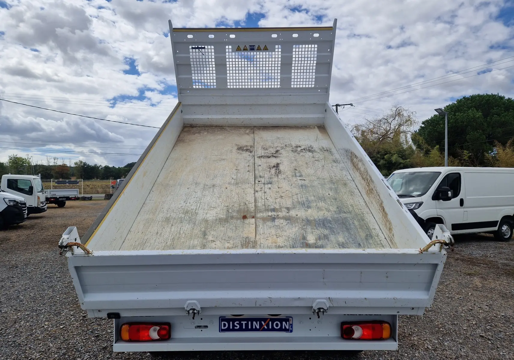 Vue arrière d’une benne blanche relevée d’un Renault Master Châssis Cabine 2024 avec roues jumelées sur un terrain extérieur.