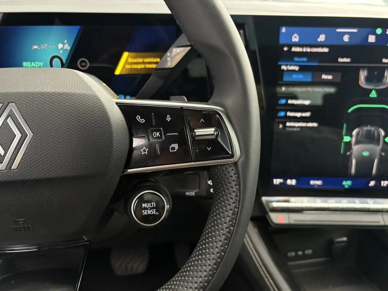 Gros plan sur le volant noir perforé du Renault Austral E-Tech avec commandes et écran tactile du tableau de bord visible.