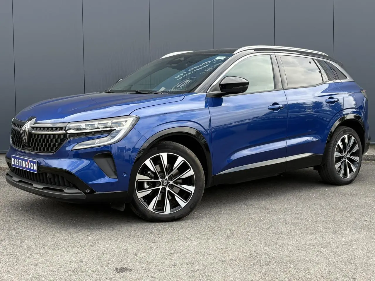 Renault Austral E-Tech bleu Iron en 3/4 avant droit, avec jantes alliage noires et toit panoramique noir étoilé.