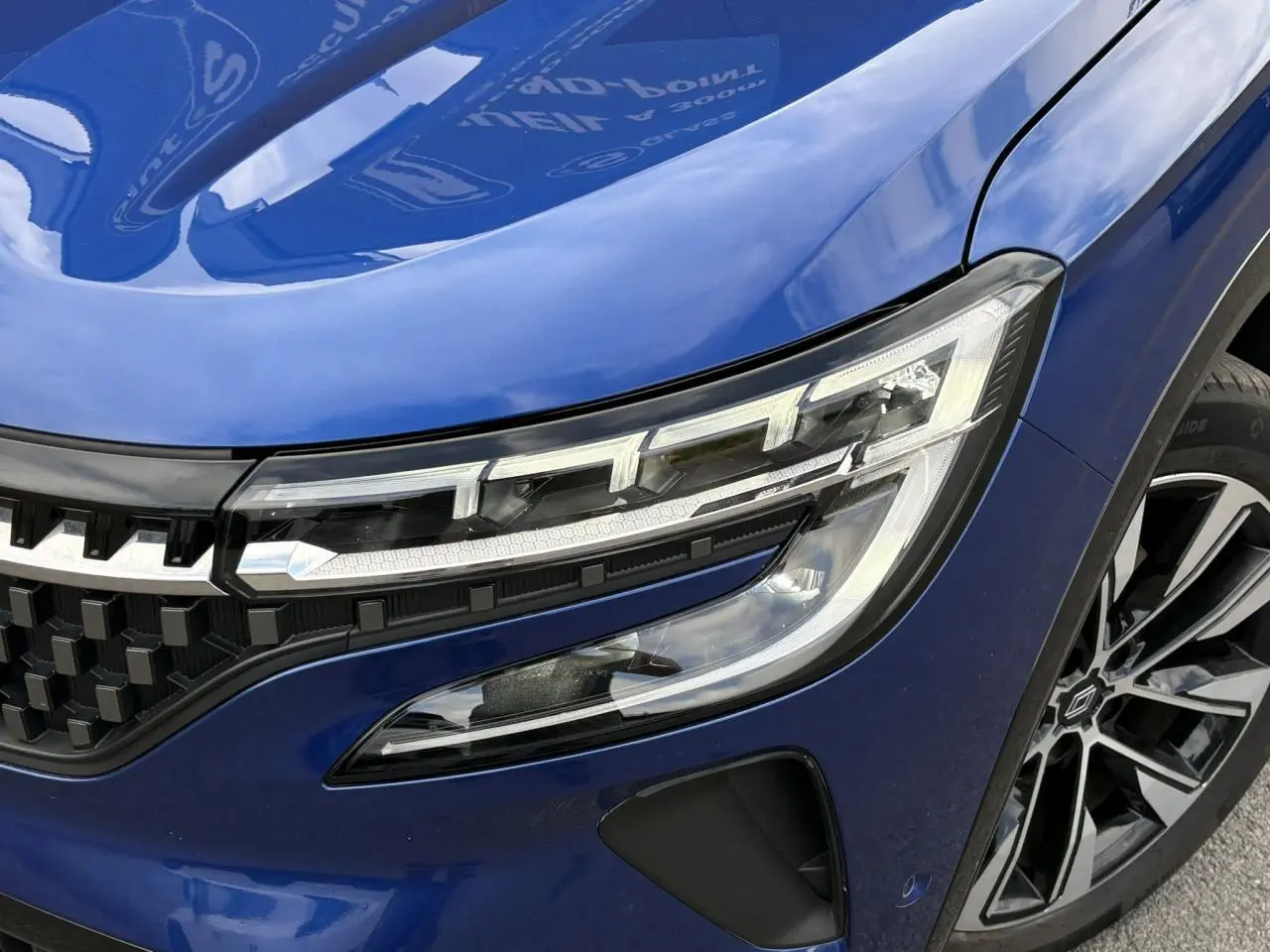 Gros plan sur l'avant droit du Renault Austral Bleu Iron, mettant en valeur le phare LED et la jante alliage noire diamantée.