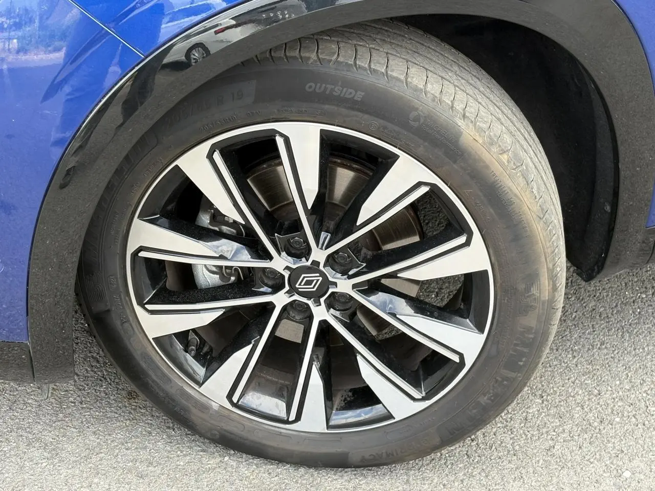 Gros plan sur la jante alliage 19 pouces diamantée noire du Renault Austral Bleu Iron, avec partie de l'aile avant visible.