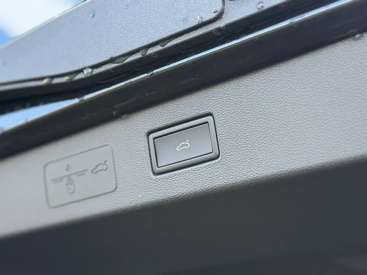 Gros plan sur le bouton d'ouverture électrique du hayon du Volkswagen T-Roc noir Ébène, intérieur du coffre visible.