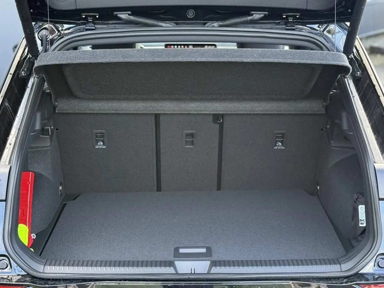 Coffre ouvert vu de l'arrière d'un Volkswagen T-Roc noir Ébène, intérieur du coffre gris avec cache-bagages relevé.