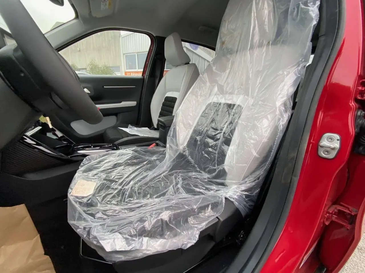 Vue intérieure côté conducteur du Citroën C3 Aircross 2025 rouge Elixir, siège avant protégé par housse plastique.