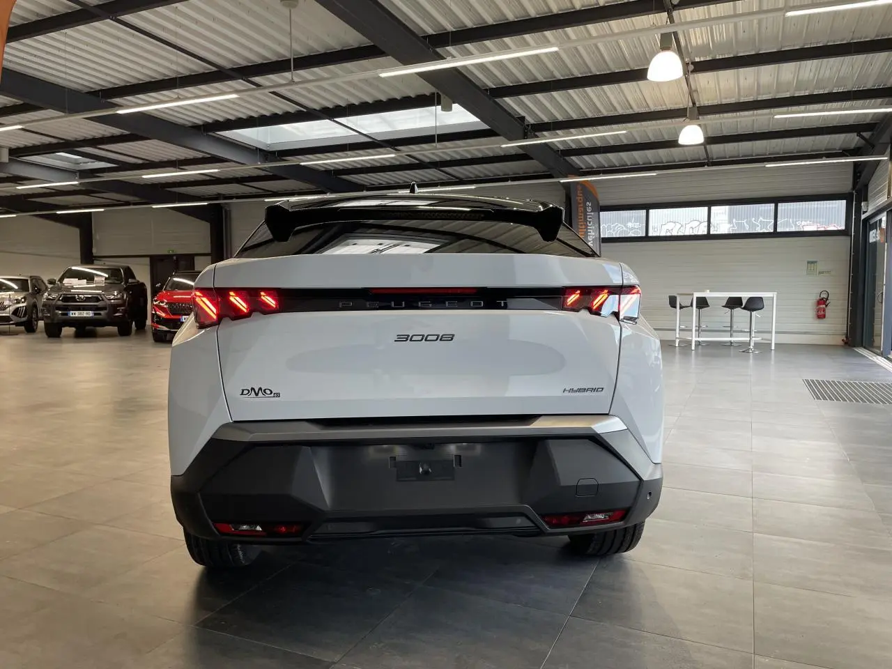 Vue arrière d'un Peugeot 3008 blanc Okenite hybride 2025 avec feux arrière à griffes LED et bandeau noir laqué.