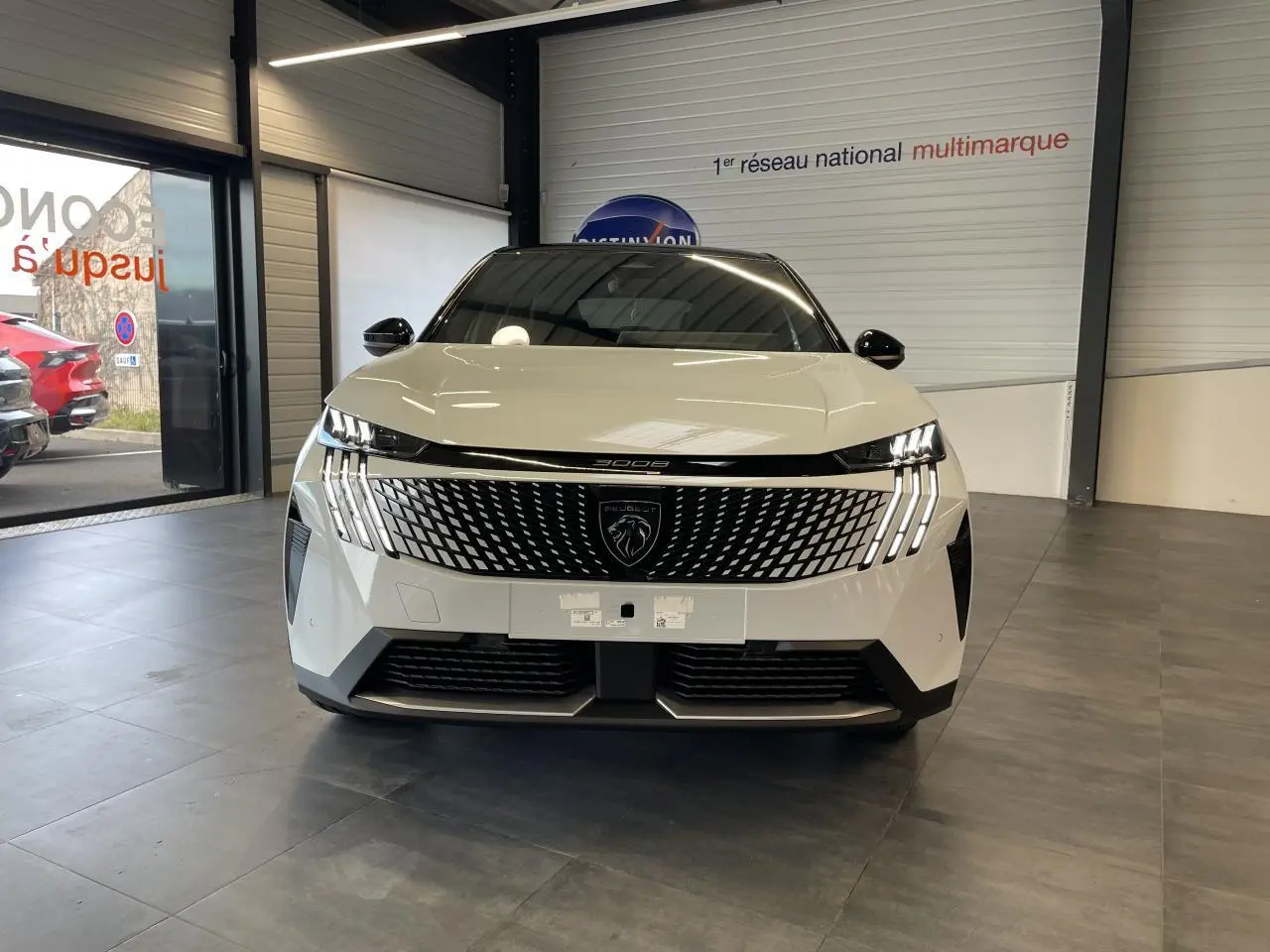 Vue frontale d'un Peugeot 3008 blanc Okenite avec calandre moderne et feux LED griffés en showroom.
