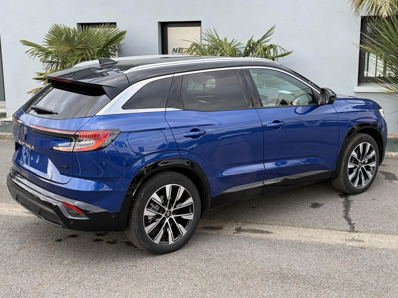 Vue 3/4 arrière droite du Renault Austral bleu Iron avec toit noir panoramique et jantes alliage noires diamantées.