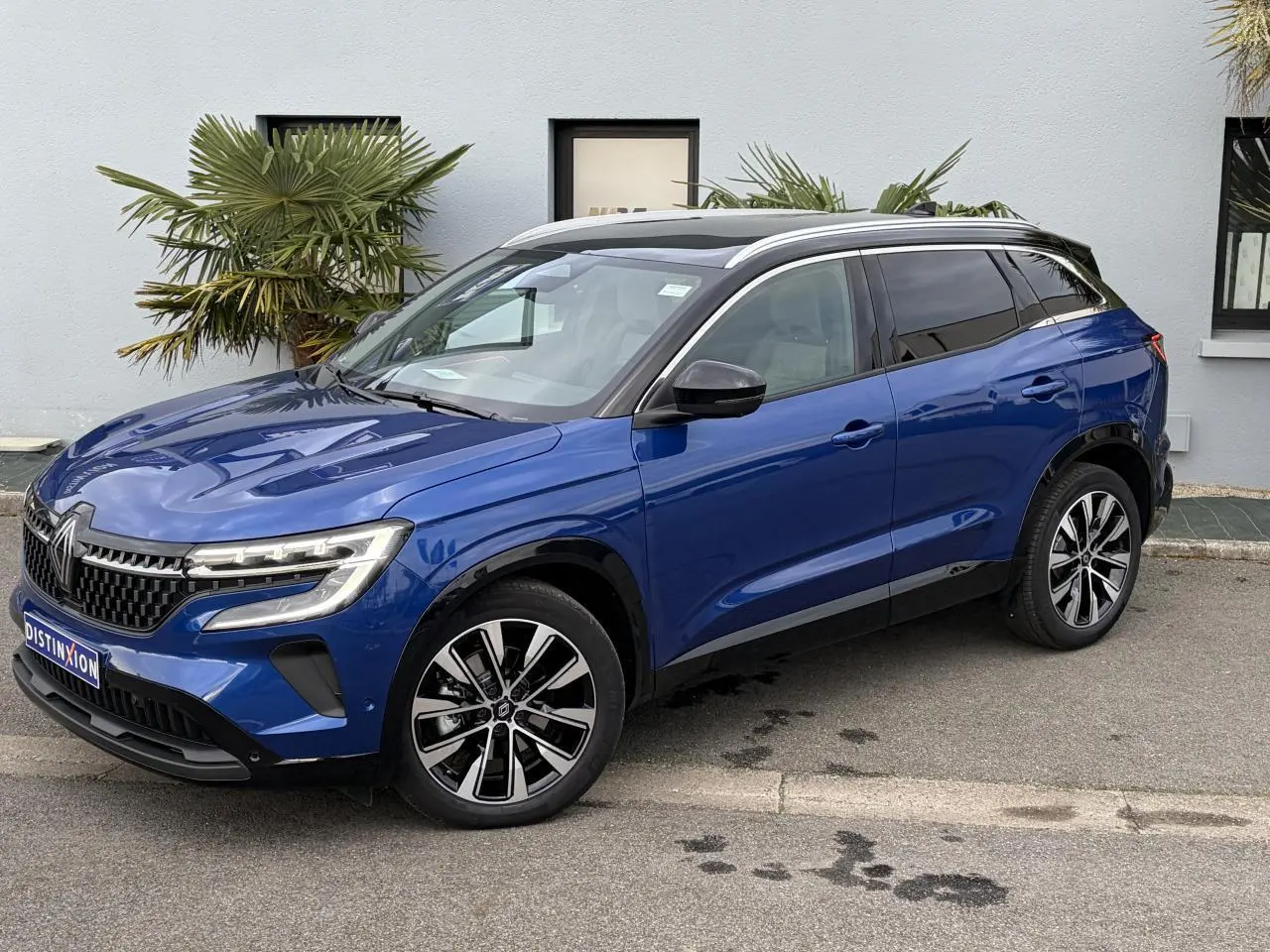 Renault Austral E-Tech hybride bleu Iron avec toit noir panoramique, vue 3/4 avant droit sur parking urbain.