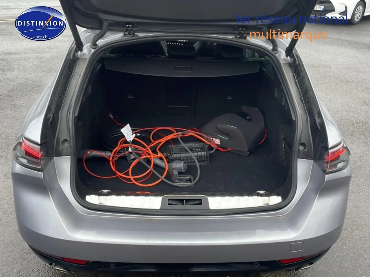 Coffre ouvert vu de l’arrière d’une Peugeot 508 SW gris artense avec câble de recharge hybride visible.