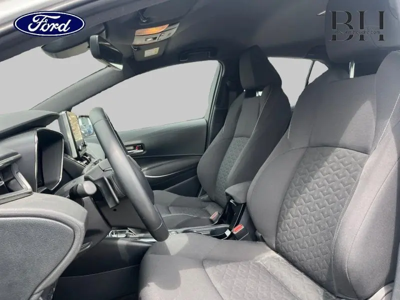 Vue intérieure côté conducteur de la Toyota Corolla 184h Dynamic Business 2022 avec sièges tissu noir et volant cuir.