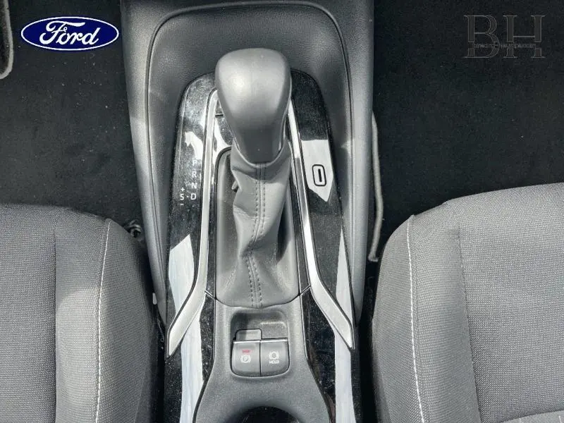 Vue plongeante sur la console centrale noire avec levier de vitesses automatique et sièges tissu gris.