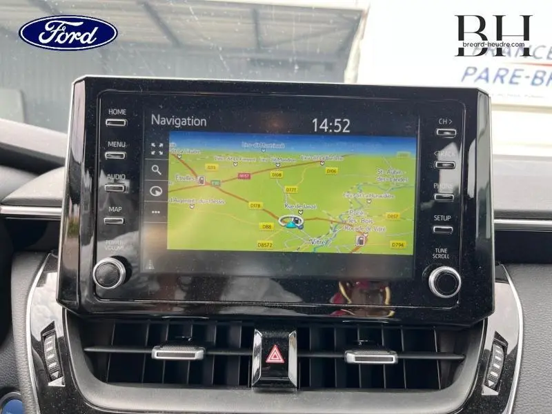 Vue rapprochée de l'écran tactile de navigation de la Toyota Corolla blanche, avec commandes latérales et ventilation en dessous.