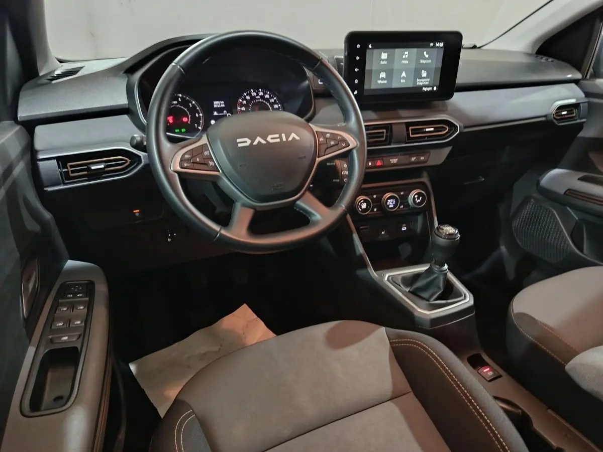 Vue intérieure avant de la Dacia Sandero 2024, tableau de bord noir avec écran tactile et volant multifonctions en cuir.