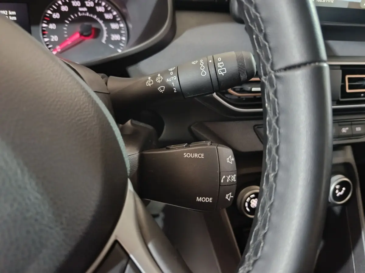 Gros plan sur la commande multifonction noire à gauche du volant cuir noir dans l'habitacle de la Dacia Sandero verte 2024.